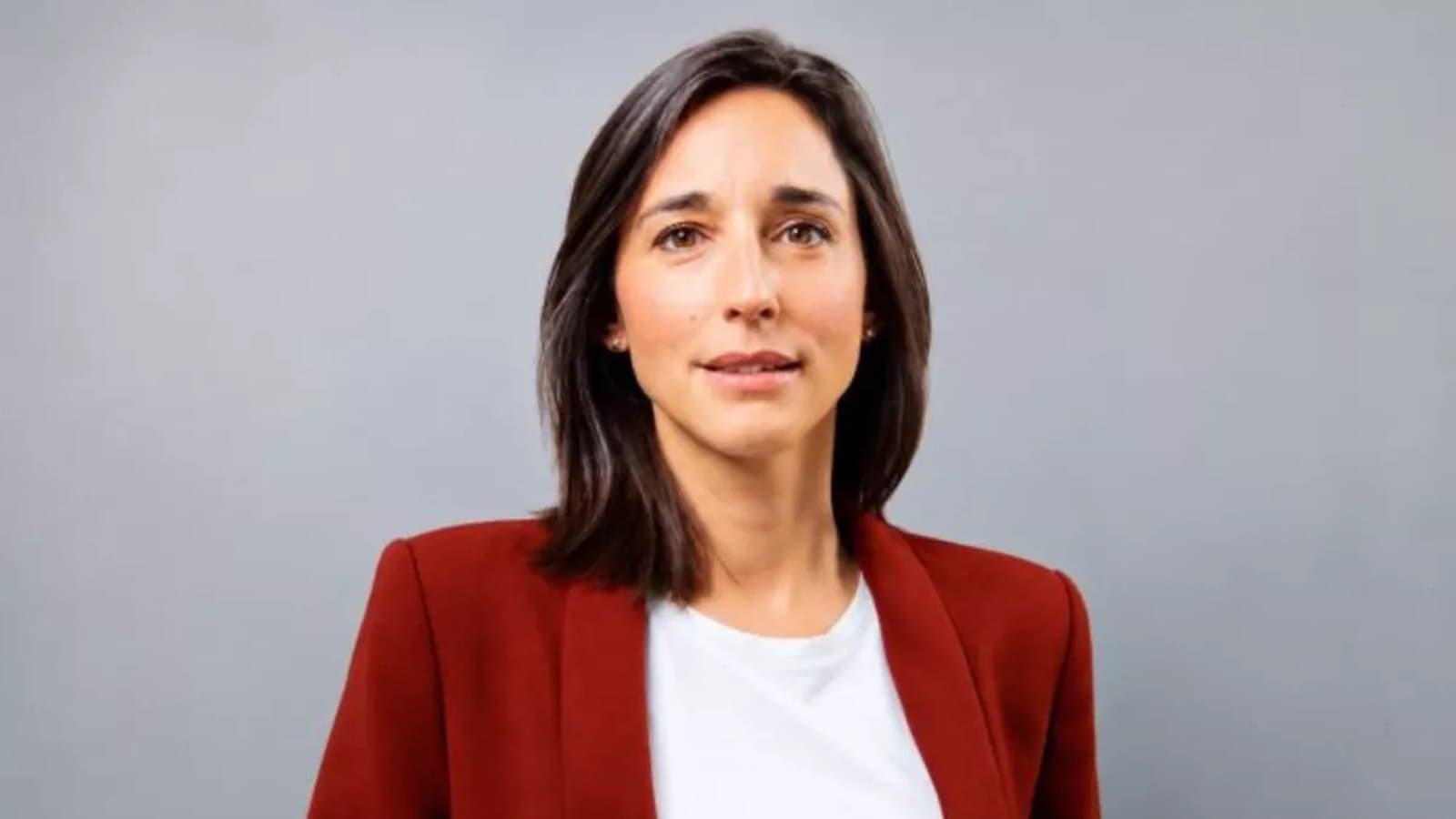 A portrait of Brune Poirson, wearing a burgundy blazer over a white top, against a plain grey background.