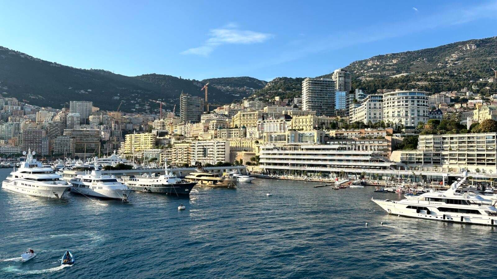 An aerial view of Monaco's harbour and hillside skyline, with superyachts moored along the marina.