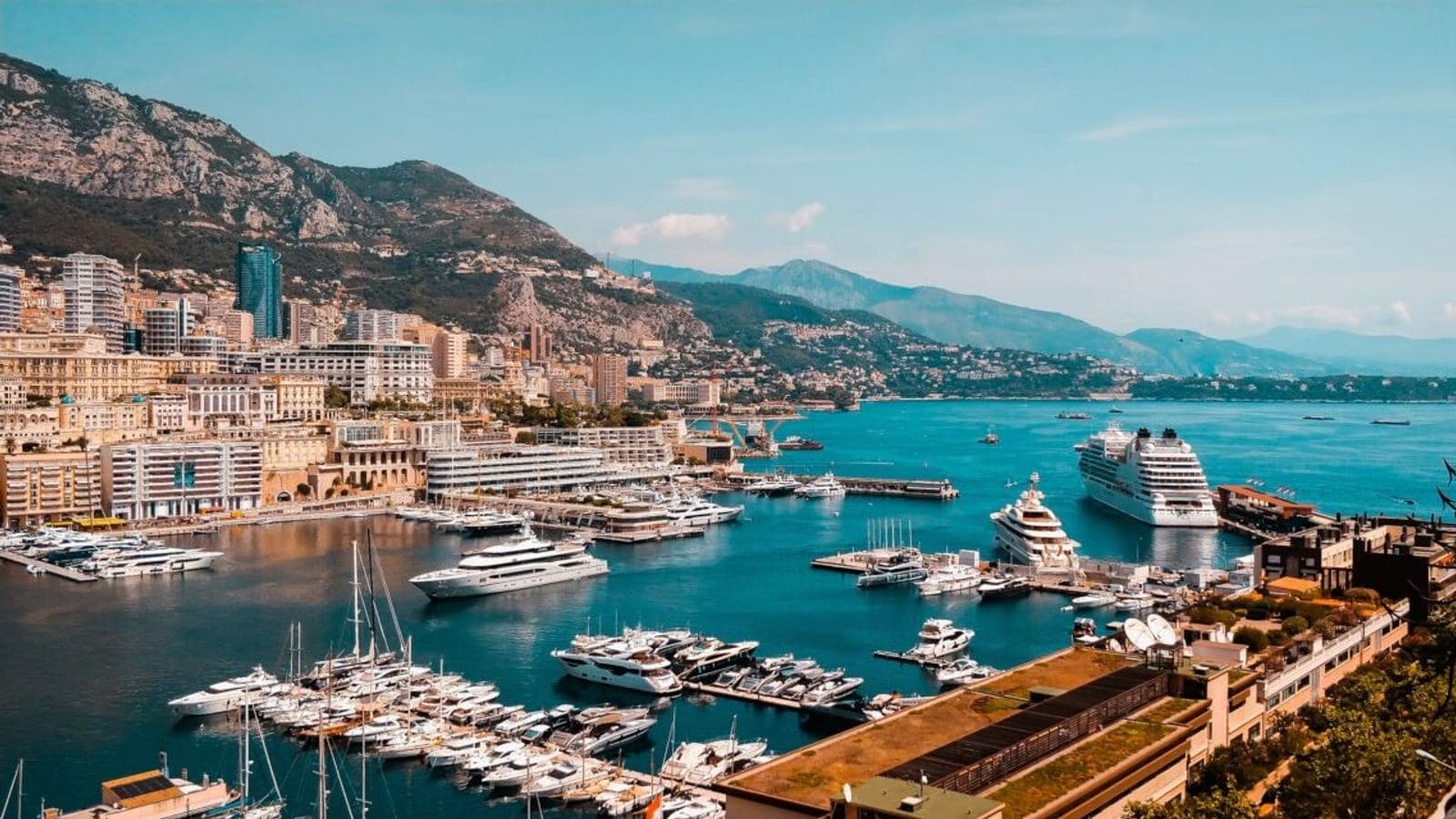An aerial view of Monaco's harbour, with superyachts and a cruise ship moored among the marina's smaller boats.
